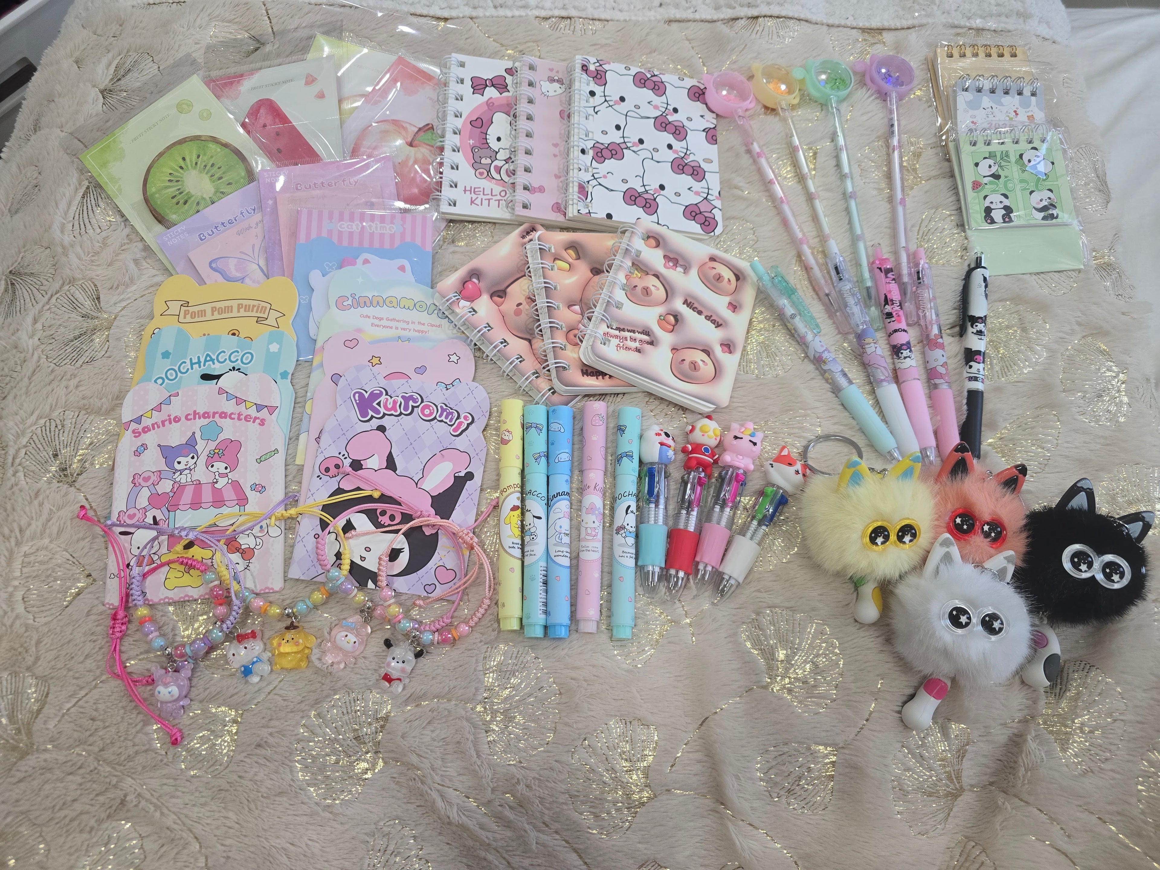 Collection of stationery items including pens, stickers, and keychains on a textured surface.